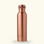 Image showcasing the Art of Vedas Copper Glass Bottle Set, featuring a 950ml copper bottle with a smooth, shiny finish and two complementary copper glasses, all arranged on a wooden table. The set reflects a warm, amber glow, emphasizing its elegant and traditional design suitable for health-focused hydration. Shop Ayurveda Oral Care Online