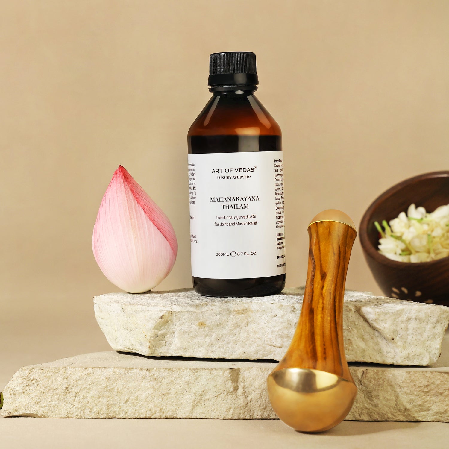 Bottle of Art of Vedas Ayurvedic oil on a stone surface with a pink lotus, wooden spoon, and bowl of flowers.