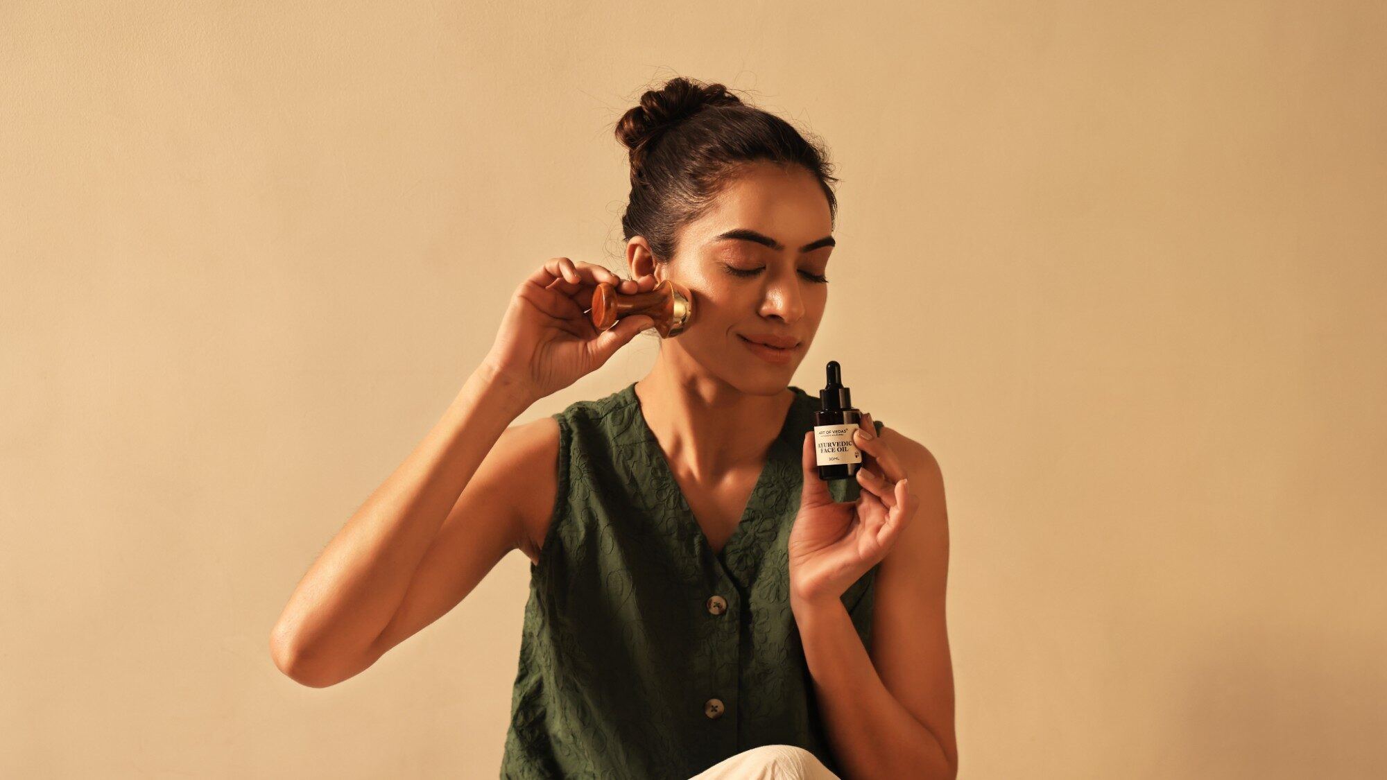 Woman using a Kansa face wand on her cheek while holding Art of Vedas Ayurvedic Face Oil